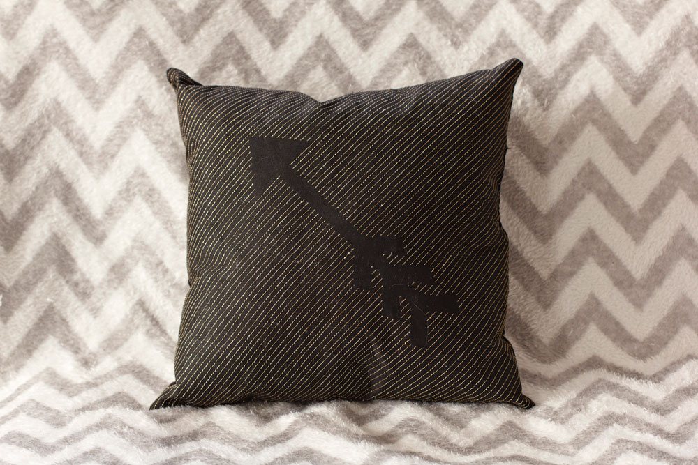 Black throw pillow with diagonal gold stitching and an arrow left unstitched in the center