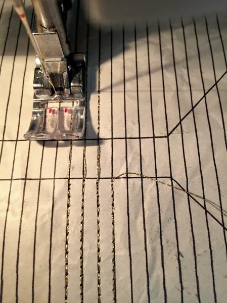 Sewing machine foot stitching gold lines over a paper pattern